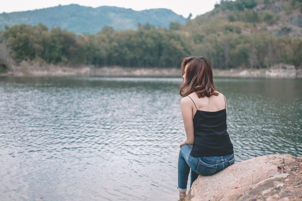 Young woman sitting on a rock by a lake.