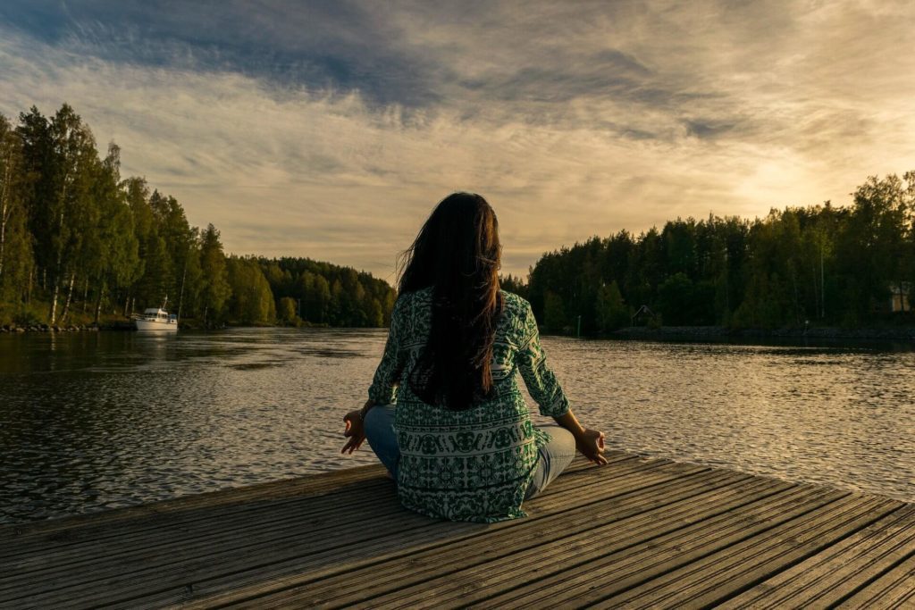 Woman meditation on a dock near a lake.